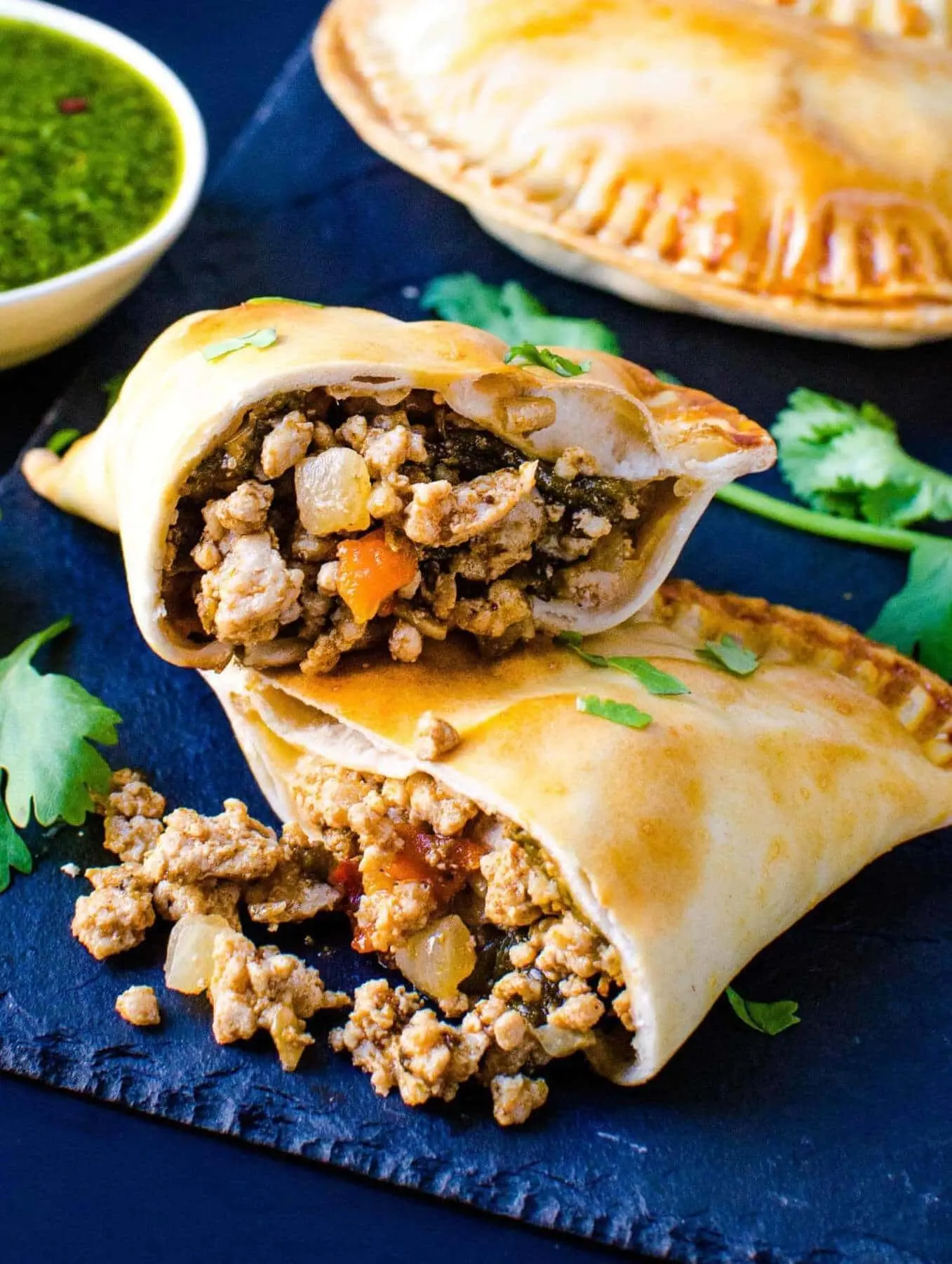 a sisig empanada cross-section view with a side of green sauce and herbs on top